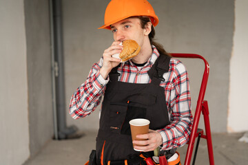 Construction Worker Eating Burger and Drinking Coffee During Lunch Break at Building Site