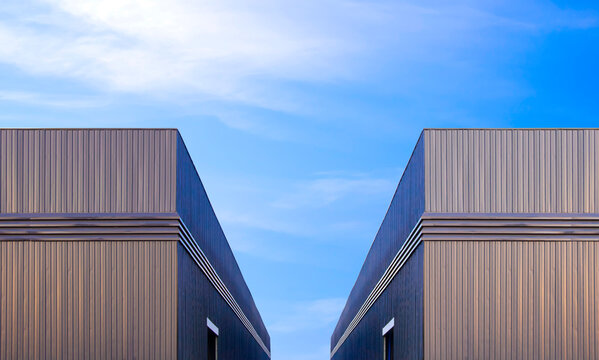 Two industrial warehouse factory buildings with ventilation louver on black corrugated metal wall against blue sky background, symmetric view with copy space