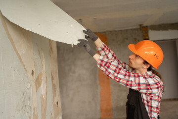 builder repairman in helmet removing old wallpaper from wall preparing apartment for renovation and interior update