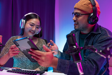 Two young asian streamer host making live podcast with condenser microphone and tablet at broadcast...