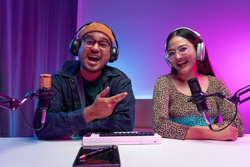 Two young asian streamer host making live podcast with condenser microphone and tablet at broadcast...