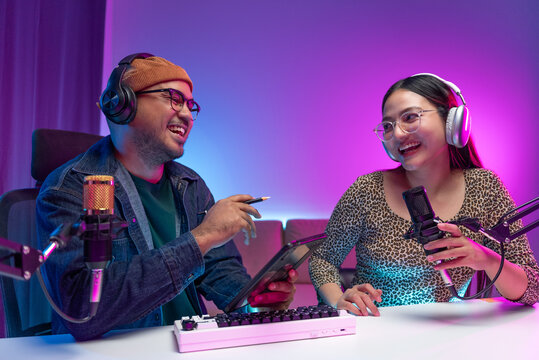 Two young asian streamer host making live podcast with condenser microphone and tablet at broadcast home studio. Content creator and social media influencer creating digital content. - Powered by Adobe