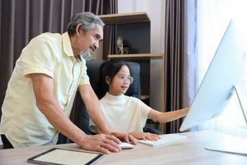 Young asian schoolgirl is doing her class homework assignment at home with advice from grandfather for education and study