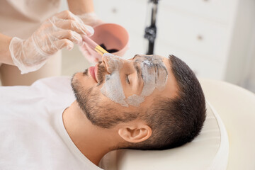 Beautician applying cosmetic bubble mask on handsome man's face in spa salon