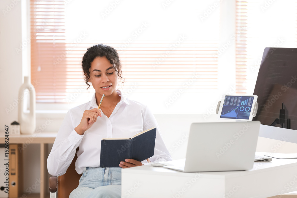 Poster young african-american qa engineer with notebook at her workspace in office