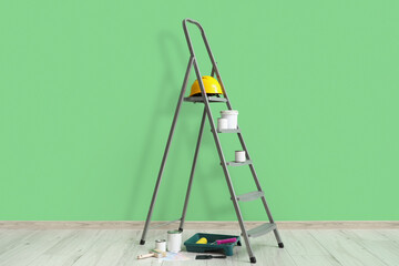 Stepladder with cans of paint and tools near green wall