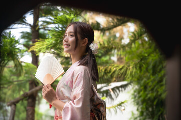 Beautiful young Japanese woman in traditional  kimono or yukata clothing holding paper fan in garden