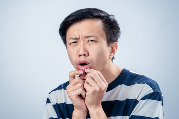 Asian man in striped shirt close-up showing a confused expression, raising eyebrows and touching...