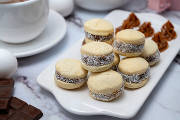 Counter with ingredients: eggs, flour, beaters, and cornstarch alfajores with dulce de leche and coconut, chocolate bar with white dishes