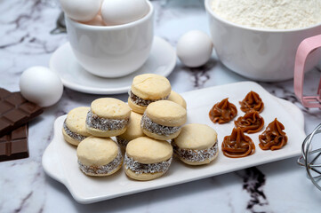 Counter with ingredients: eggs, flour, beaters, and cornstarch alfajores with dulce de leche and coconut, chocolate bar with white dishes