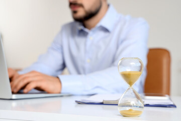 Hourglass on desk against businessman working with laptop in office, closeup