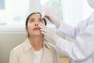 Health care concept, eye doctor eye drops to asian young woman patient, hand using medical eye drop...