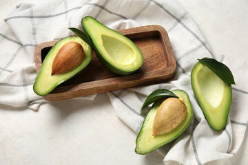 Wooden tray with halves of fresh ripe avocados on white background