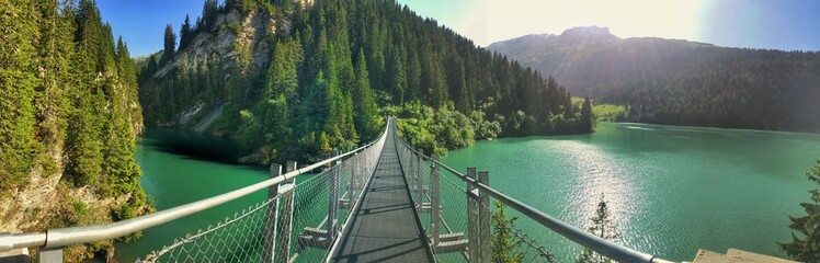Panoramic view of a suspension bridge over a serene forested mountain lake