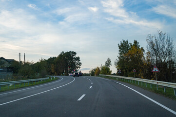Winding road through autumnal landscape near quiet rural town during late afternoon