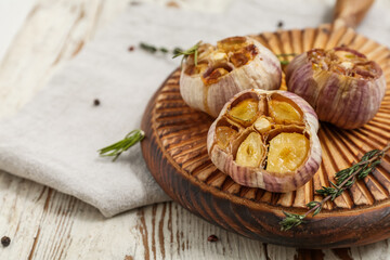 Board with baked garlic, rosemary, peppercorns and thyme on beige wooden background