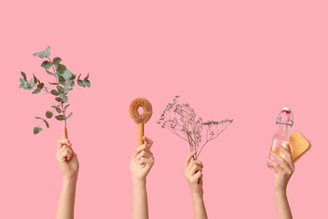 Female hands with bottle of detergent, sponges and plant branches on pink background