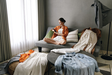 Cozy indoor scene with a young woman in a stylish outfit organizing her clothing on a gray sofa, emphasizing modern lifestyle and fashion