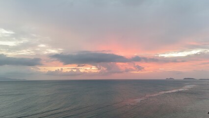 Beautiful cloudy red sunrise over sea with beach, waves and mountains in the background. Impressive structure texture in the sky