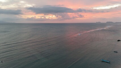 Beautiful cloudy red sunrise over sea with beach, waves and mountains in the background. Impressive structure texture in the sky