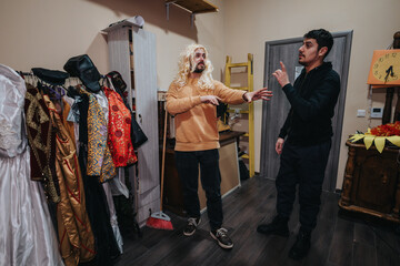 Two actors in a theater's costume room rehearsing a scene, surrounded by colorful outfits and...