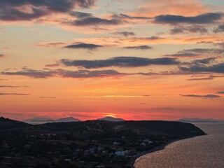 Beautiful cloudy red sunrise over sea with beach, waves and mountains in the background. Impressive structure texture in the sky