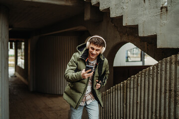 Young adult caucasian man student smile with phone and headphones on university stairs
