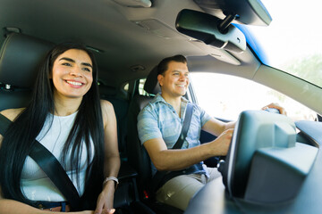 Happy couple driving modern car wearing seatbelts on road trip