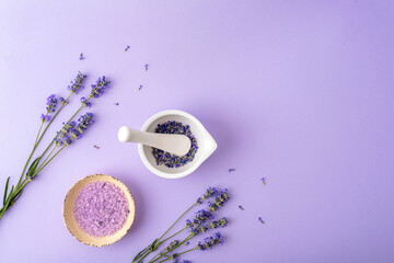 Mortar and pestel with lavender flowers and bath salt in a bowl on purple background. Natural herbs medicine concept. Top view, flat lay