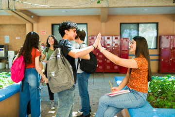 Happy high school students giving high five in school hallway