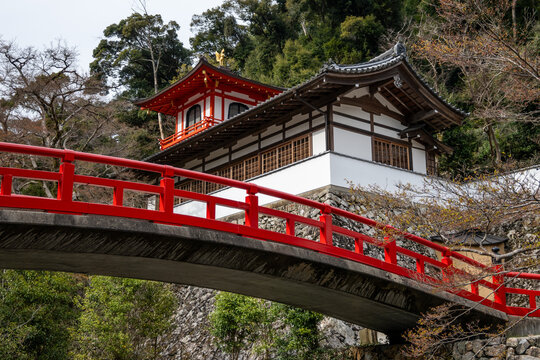 A picturesque Japanese temple nestled on a hillside, featuring a vibrant red bridge in Minoh National Park, Osaka, Japan. It evokes the serenity of ancient Buddhist pract
