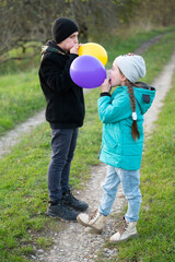 Kids enjoy a delightful moment blowing up colorful balloons on a sunny afternoon in the park, creating joyful memories along the winding pathway surrounded by nature