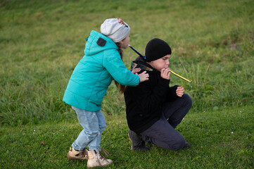 Children playing a joyful game outdoors while one blows a colorful toy whistle in a green grassy...
