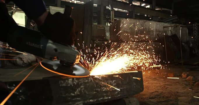 Male hand cuts off pieces of water pipe with angle grinder. Cutting of a steel with splashes of sparks at construction site. Sparks during cutting of metal angle grinder