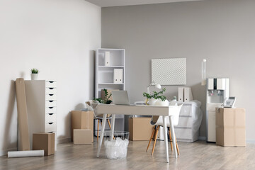 Interior of office with workplace, water cooler and cardboard boxes on moving day
