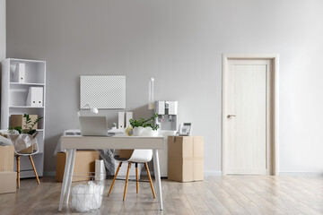 Interior of office with workplace, shelf unit and cardboard boxes on moving day