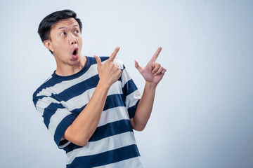 Asian man in a striped shirt enthusiastically pointing to the right with both hands, smiling and...