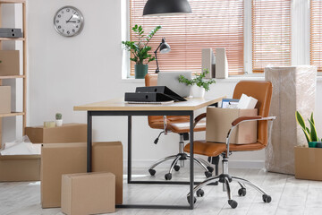 Interior of office with workplace, plants and cardboard boxes on moving day