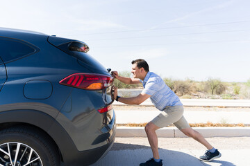 Frustrated driver pushing broken car on highway