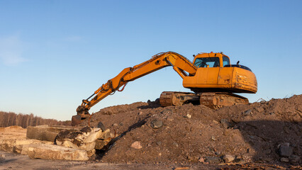 Yellow excavator groundworks on sunset, digger on construction site on blue sky. Heavy construction equipment on excavation on construction site, open-pit mining