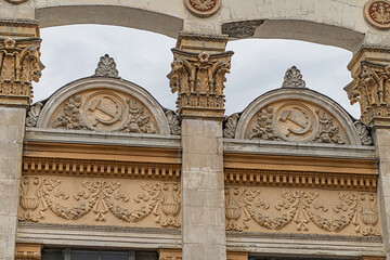 Stone Soviet architecture, grand design with arches, cupolas, columns, and possible pediments Emblematic symbol on one arch hammer sickle, star, wheat sheaves in red gold Historical public or