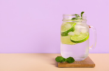 Mason jar of fresh Mojito cocktail with mint on beige table against lilac background
