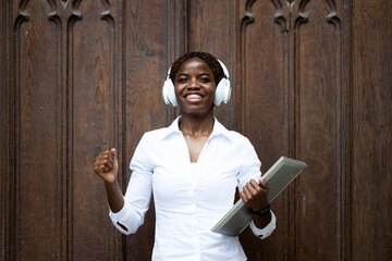 Portrait of smiling African female student with laptop computer standing by university building door.