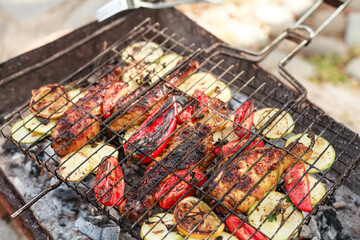 Grilling vegetables, sausages, and trout over charcoal in a backyard during summer. Outdoor cooking with real flames and smoke in a cozy home setting