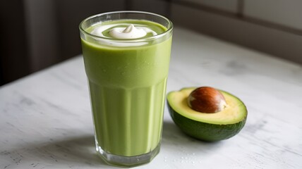 Avocado smoothie with fresh milk in a clear glass with avocado on the side of the glass on a white background.