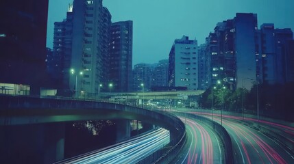Obraz premium Night city highway. Urban cityscape at twilight. Light trails from vehicles on a curving road. Buildings rise into the muted blue twilight