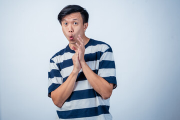Asian man in striped shirt clapping his hands with a playful and cheerful expression, standing...