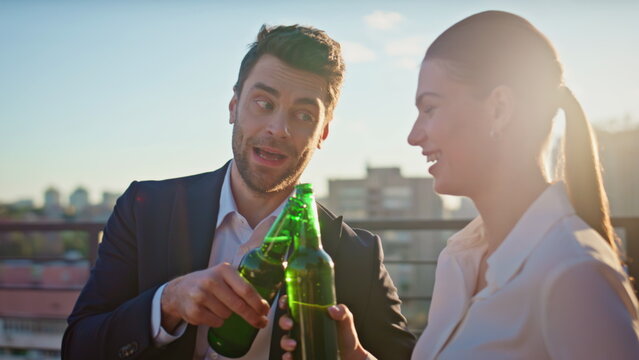 Office colleagues toasting beer bottles on summer sunset at roof closeup.