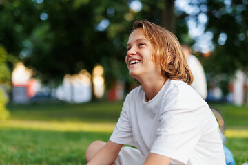 Portrait of little cute adorable happy caucasian blond boy enjoy sitting outdoors in city park or summer camp holidays on sunny warm day. Male kid laughing outside. Childhood carefree lifestyle