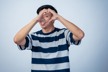 Image Description (under 195 characters):
Asian man in striped shirt smiling and forming a heart...